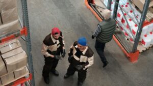 Trabajadores gestionando mercancía en almacén logístico con estanterías industriales y control de inventario.