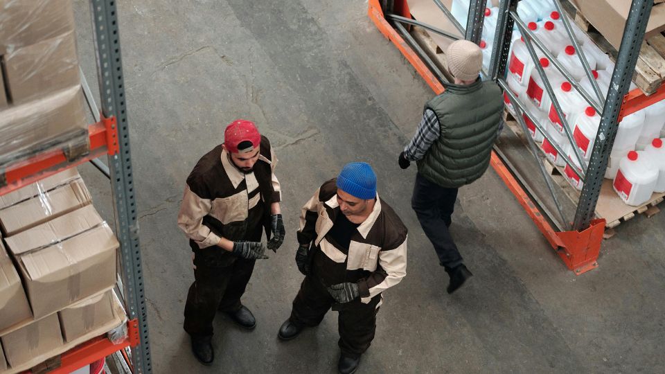 Trabajadores gestionando mercancía en almacén logístico con estanterías industriales y control de inventario.