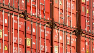 Contenedores de mercancías rojos apilados en una terminal logística, utilizados para ilustrar los factores que influyen en el precio del transporte de mercancías por carretera.