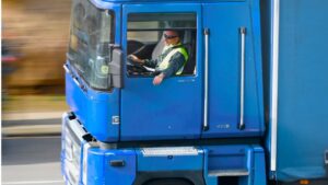 Conductor profesional al volante de un camión azul durante una jornada de transporte por carretera, relacionada con los tiempos de conducción y descanso.