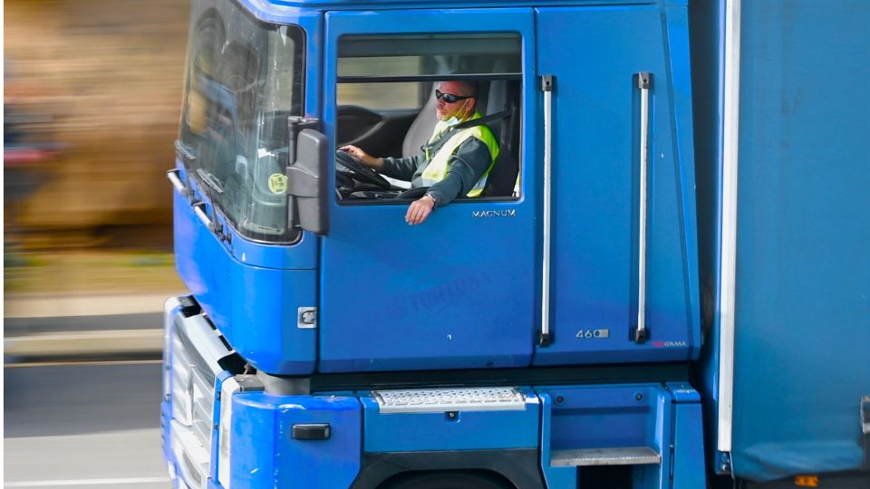 Conductor profesional al volante de un camión azul durante una jornada de transporte por carretera, relacionada con los tiempos de conducción y descanso.